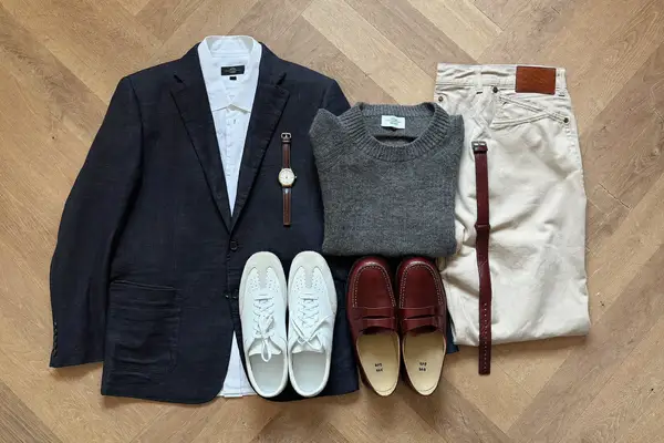 Flat lay of a men's capsule wardrobe with blazer, oxford shirt, jeans, chinos and shoes