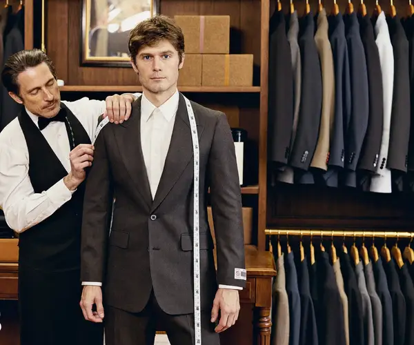 Tailor fitting a charcoal suit jacket on a man in a traditional tailoring shop