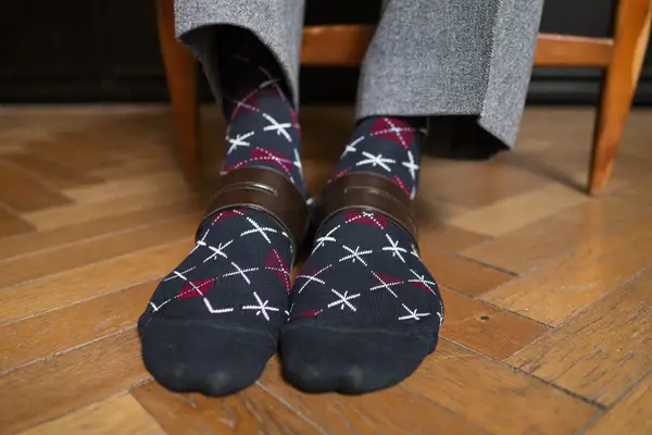 Man wearing patterned navy and burgundy dress socks with grey trousers and brown brogues