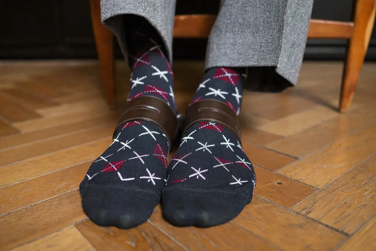 Man wearing patterned navy and burgundy dress socks with grey trousers and brown brogues