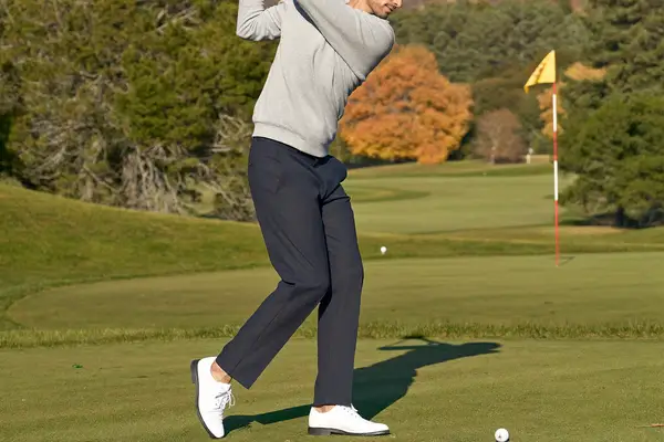 Golfer in a grey quarter-zip and navy trousers finishing a swing on an autumn golf course