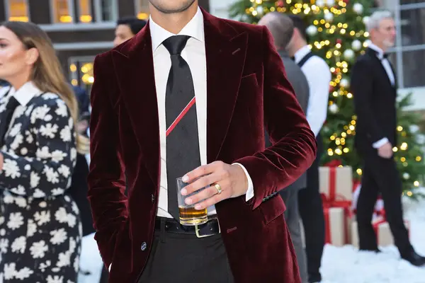 Man in a burgundy velvet dinner jacket holding a drink at a Christmas party