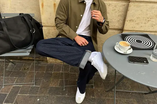 Man in an olive overshirt, white t-shirt and dark jeans at a café