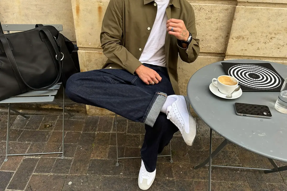 Man in an olive overshirt, white t-shirt and dark jeans at a café