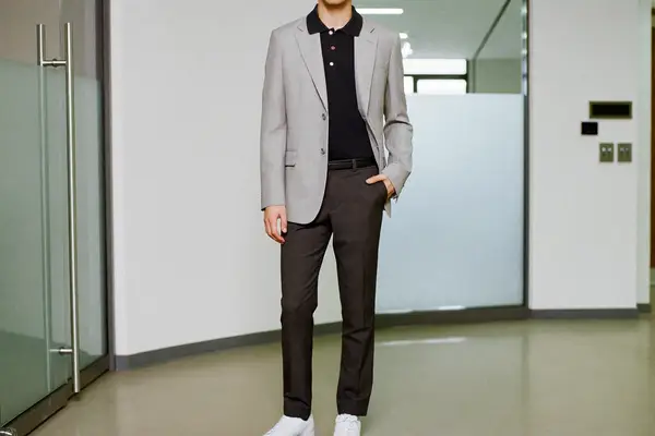 Man in a knitted polo, unstructured grey blazer, charcoal trousers and white leather sneakers